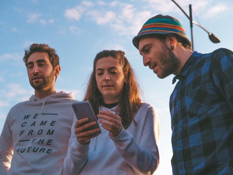 Drei Menschen schauen auf ein Smartphone. 