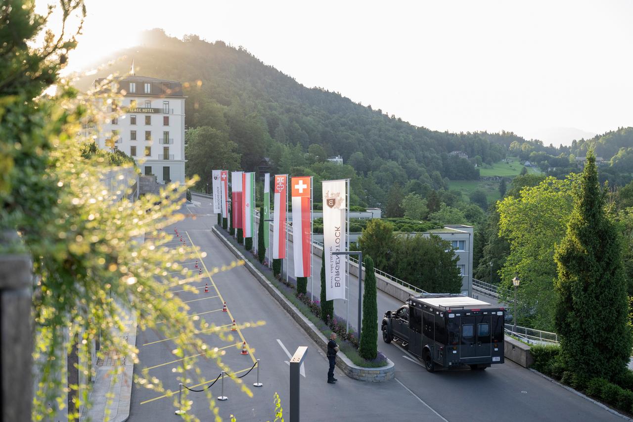 Das Bild zeigt die Zufahrt zu einem Hotel an einem Berghang. Ein Militärfahrzeug fährt auf das Hotel zu. Entlang der Zufahrt sind mehrere Flaggen gehisst, darunter die Flagge der Schweiz und Pakistans. Das Bild zeigt die Zufahrt zu einem Hotel an einem Berghang. Ein Militärfahrzeug fährt auf das Hotel zu. Entlang der Zufahrt sind mehrere Flaggen gehisst, darunter die Flagge der Schweiz und Pakistans.