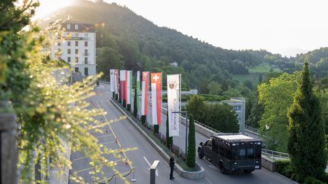 Das Bild zeigt die Zufahrt zu einem Hotel an einem Berghang. Ein Militärfahrzeug fährt auf das Hotel zu. Entlang der Zufahrt sind mehrere Flaggen gehisst, darunter die Flagge der Schweiz und Pakistans.