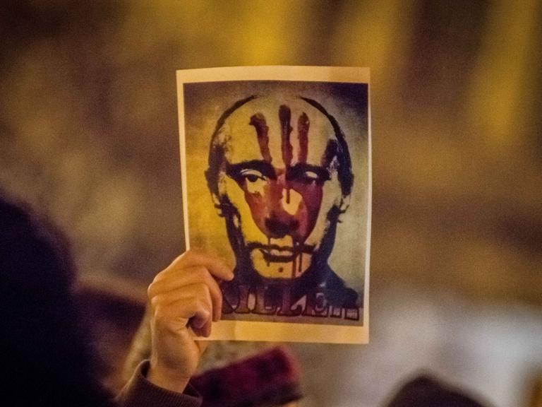 Eine Hand hält ein Bild von Putin hoch, auf dem ein blutiger Handabdruck und die Aufschrift "Killer" zu sehen ist.