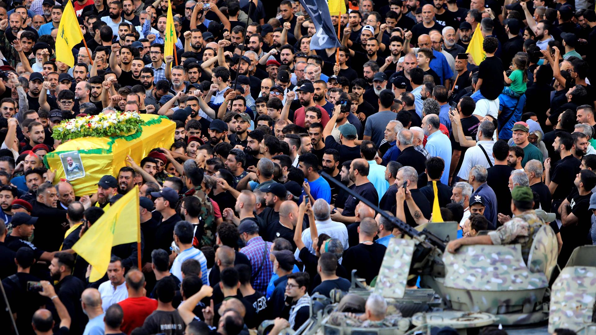 Menschen nehmen an der Beerdigung eines Opfers der im Libanon explodierten Pager teil. Links wird ein Sarg der in eine gelbe Hisbollah-Flagge gehüllt ist getragen.