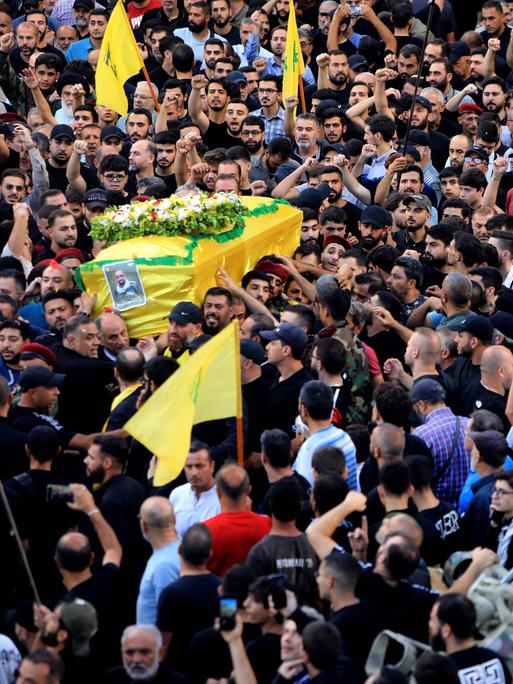 Menschen nehmen an der Beerdigung eines Opfers der im Libanon explodierten Pager teil. Links wird ein Sarg der in eine gelbe Hisbollah-Flagge gehüllt ist getragen.