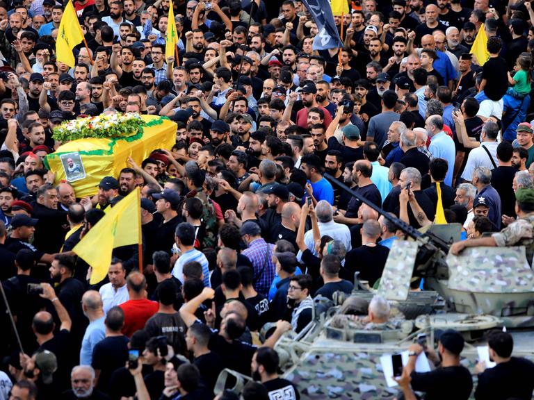 Menschen nehmen an der Beerdigung eines Opfers der im Libanon explodierten Pager teil. Links wird ein Sarg der in eine gelbe Hisbollah-Flagge gehüllt ist getragen.