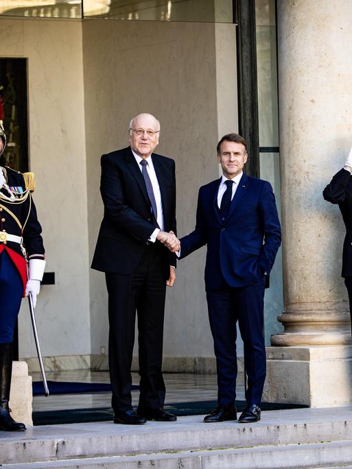 Frankreichs Präsident Emmanuel Macron schüttelt die Hand des geschäftsführenden Ministerpräsidenten des Libanons, Nadschib Mikati, daneben stehen zwei Militärangehörige