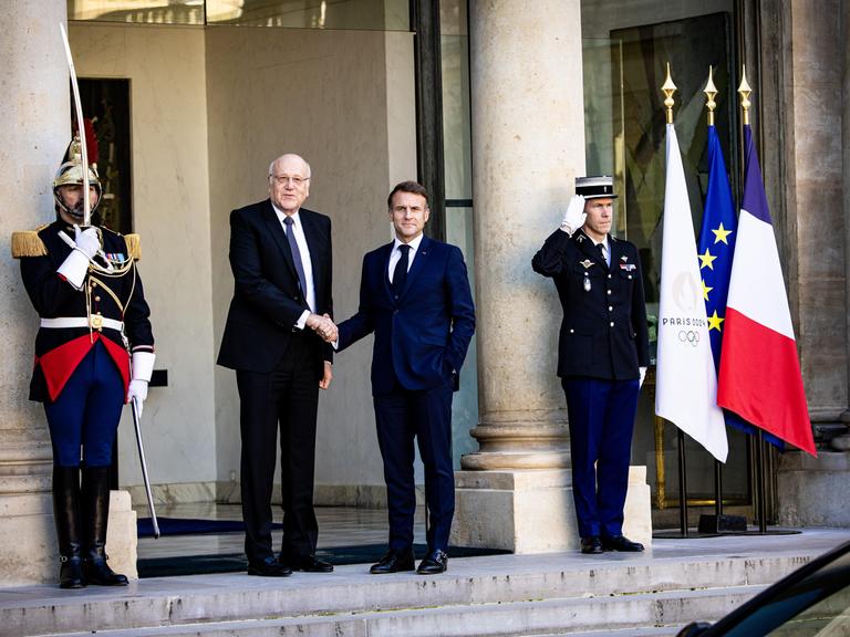 Frankreichs Präsident Emmanuel Macron schüttelt die Hand des geschäftsführenden Ministerpräsidenten des Libanons, Nadschib Mikati, daneben stehen zwei Militärangehörige