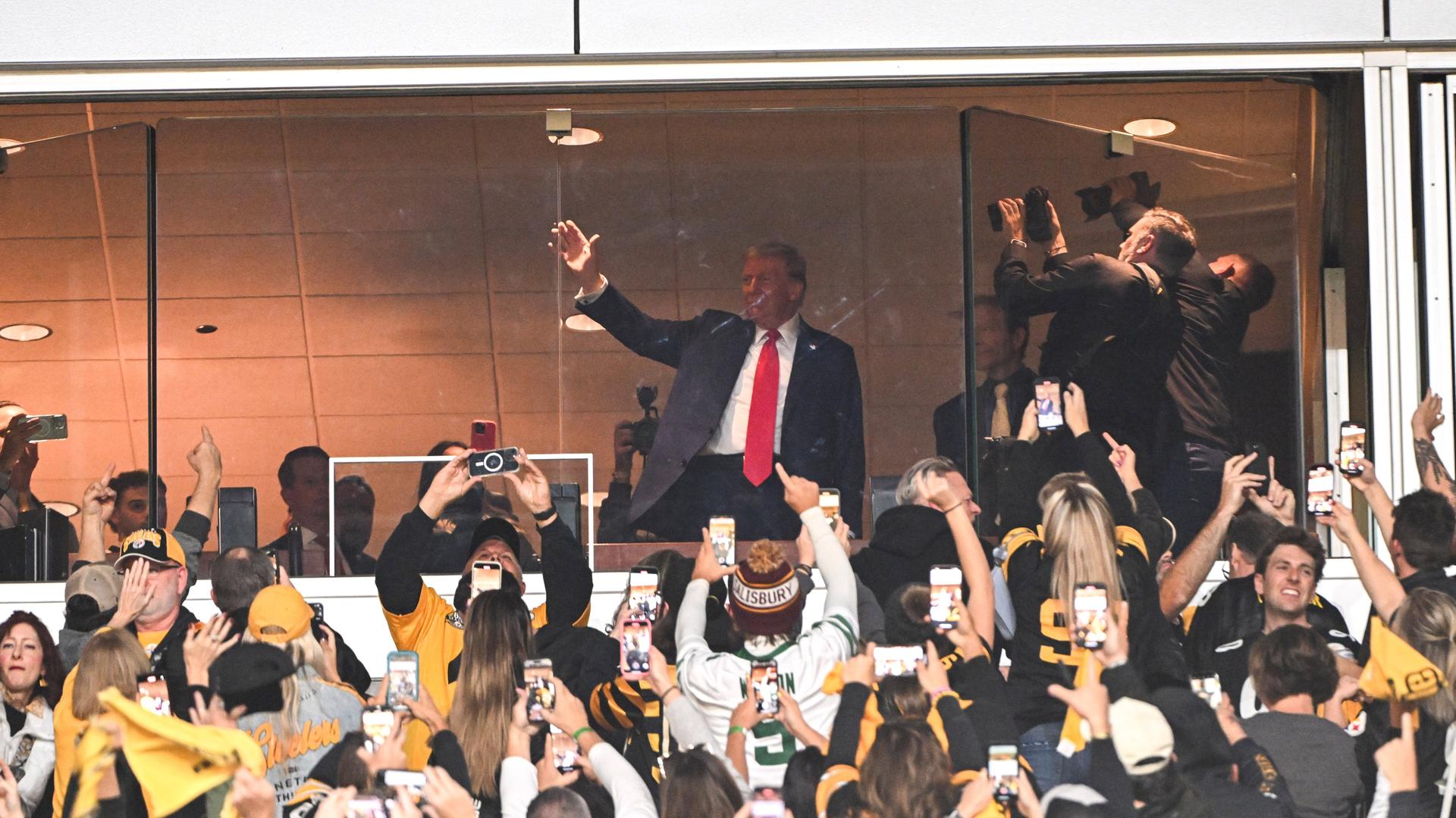 Donald Trump grüßt bei einem Eishockey-Spiel das Publikum. 