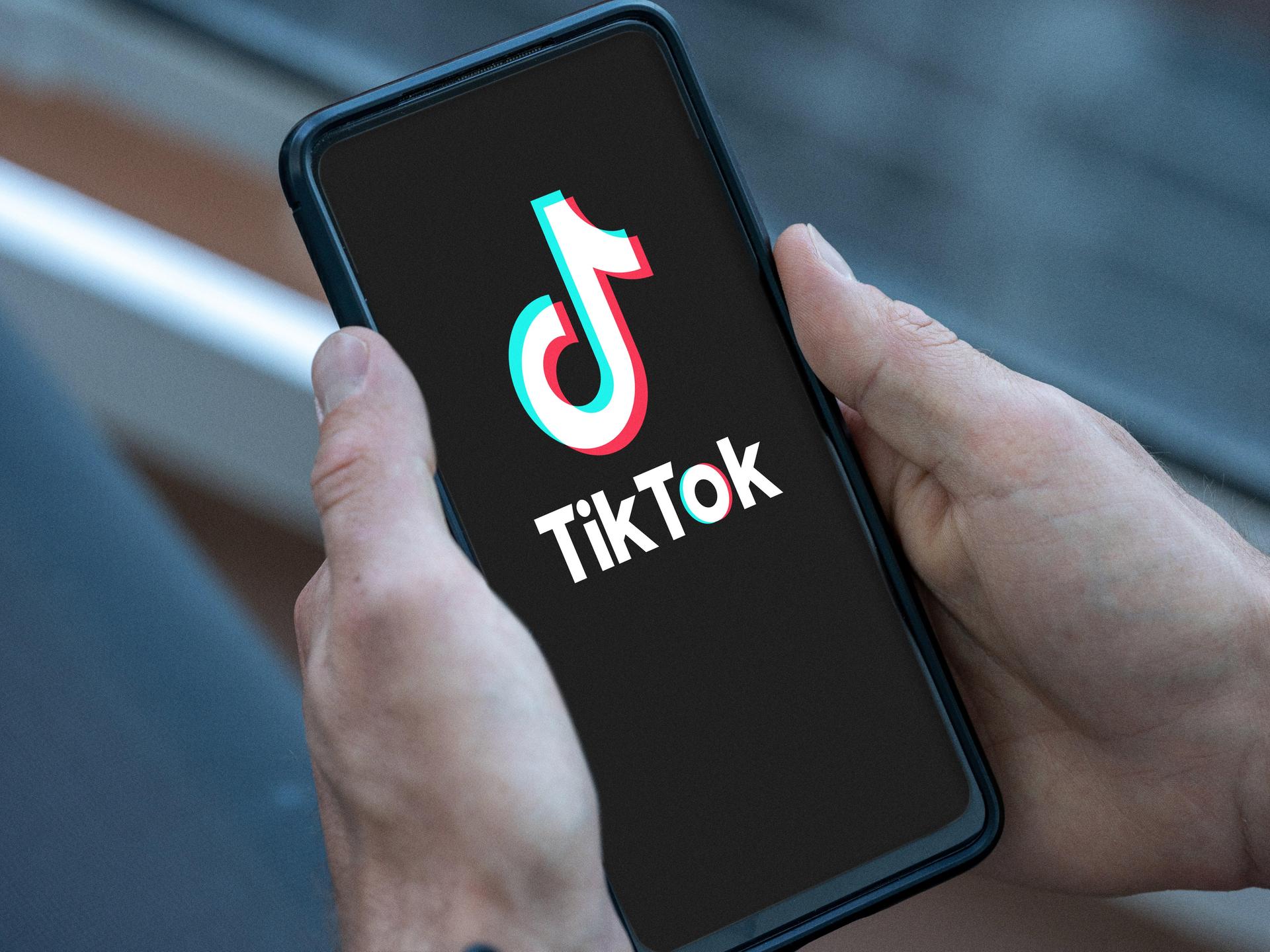Mann hält Smartphone in der Hand mit dem TikTok Logo auf dem Bildschirm.  