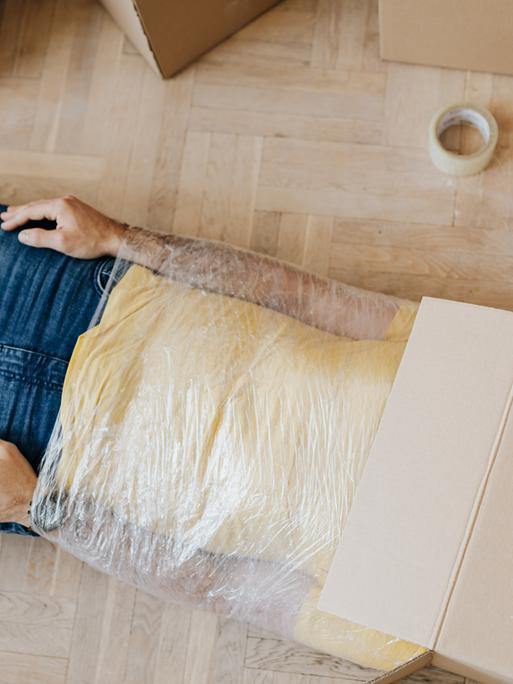 Mann liegt auf dem Boden und kann sich nicht bewegen. Er hat einen Karton auf dem Kopf. 