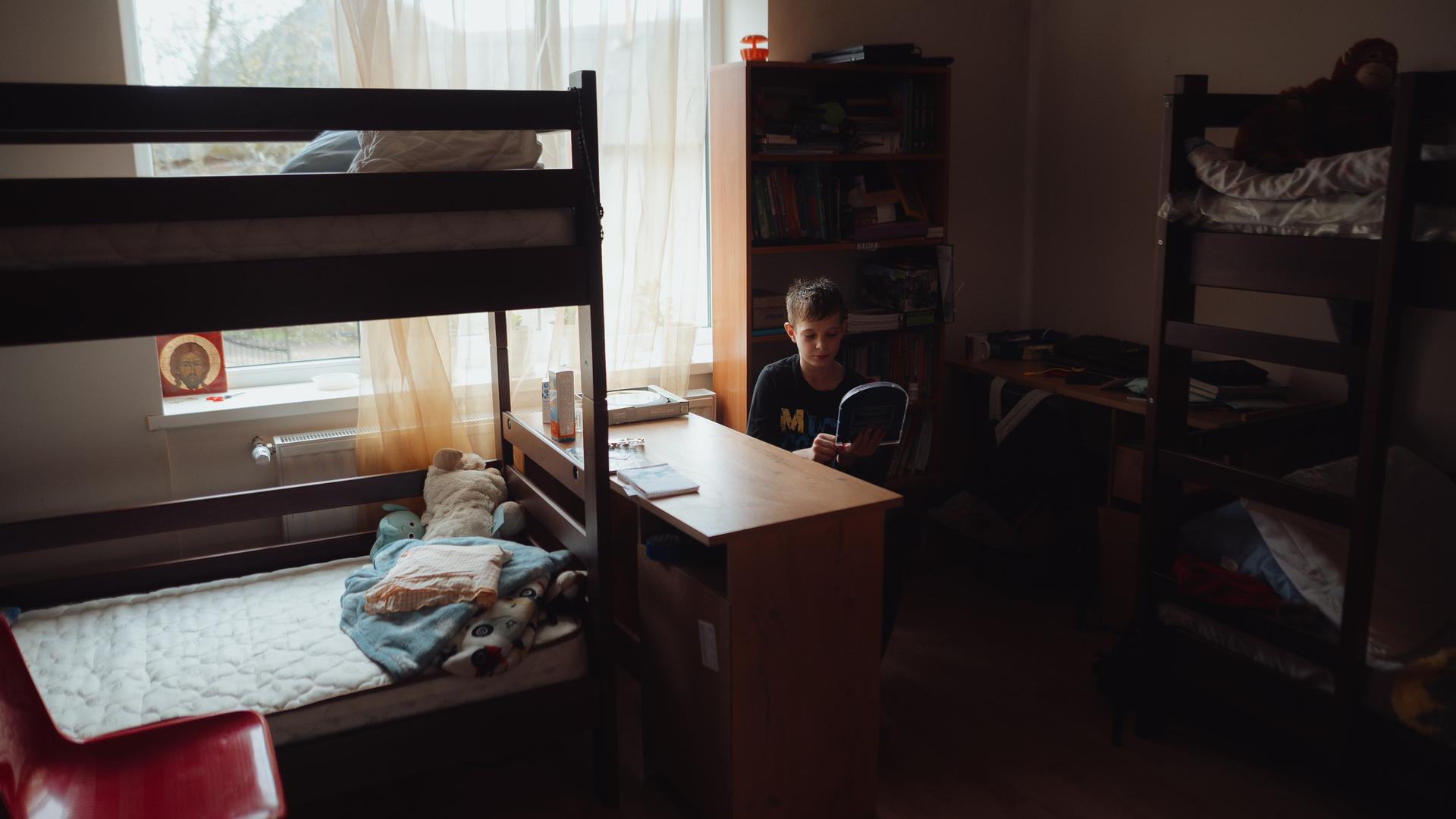 Ein Junge sitzt in einem Zimmer in einem Kinderhaus in Mariupol zwischen Stockbetten.