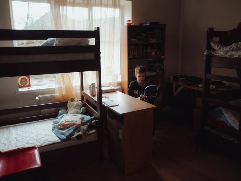Ein Junge sitzt in einem Zimmer in einem Kinderhaus in Mariupol zwischen Stockbetten.