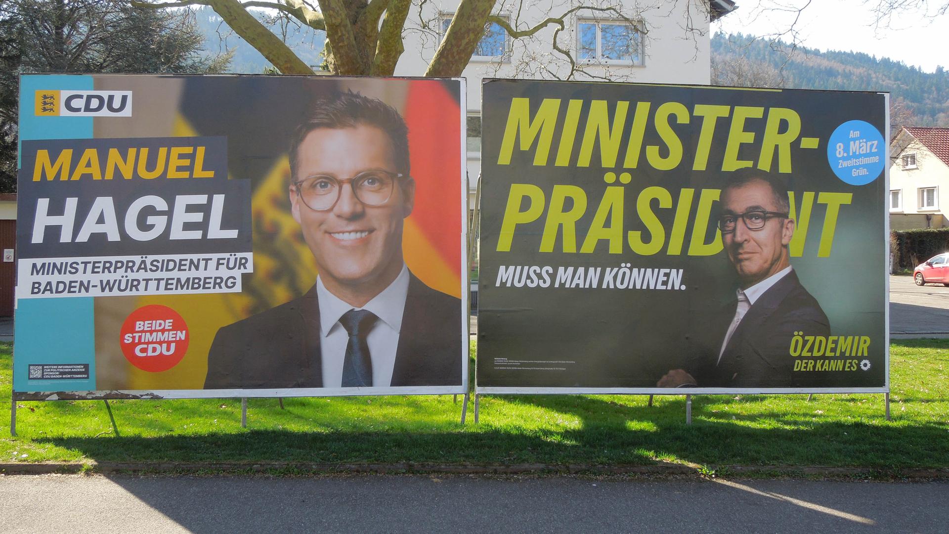 Zwei Wahlplakate der Kandidaten Manuel Hagel und Cem Özdemir vor einem Baum und einem Wohnhaus in Freiburg/Breisgau.