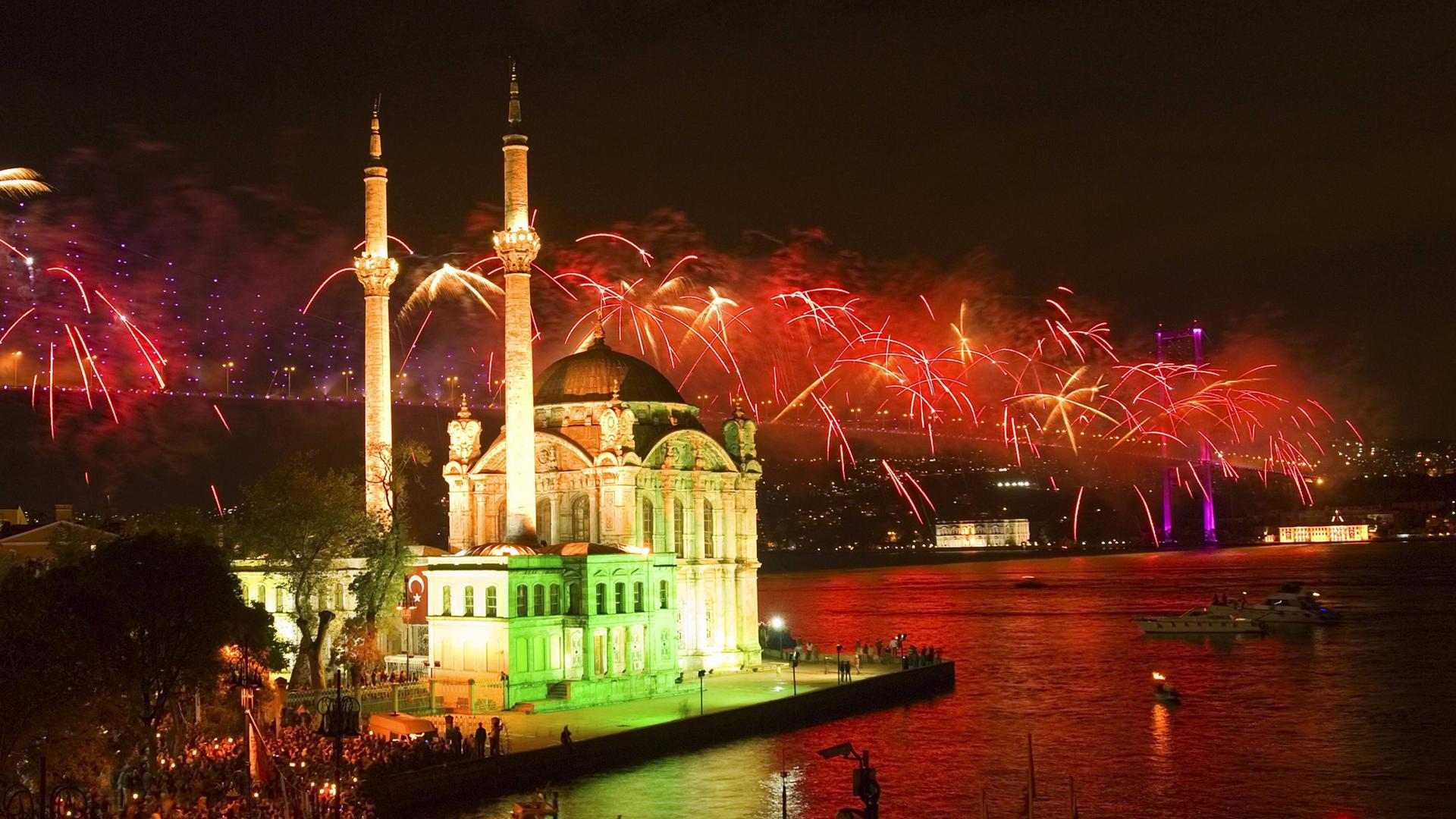 Blick auf die Ortakoy-Moschee und Bosporusbruecke bei Nacht mit Feuerwerk. 