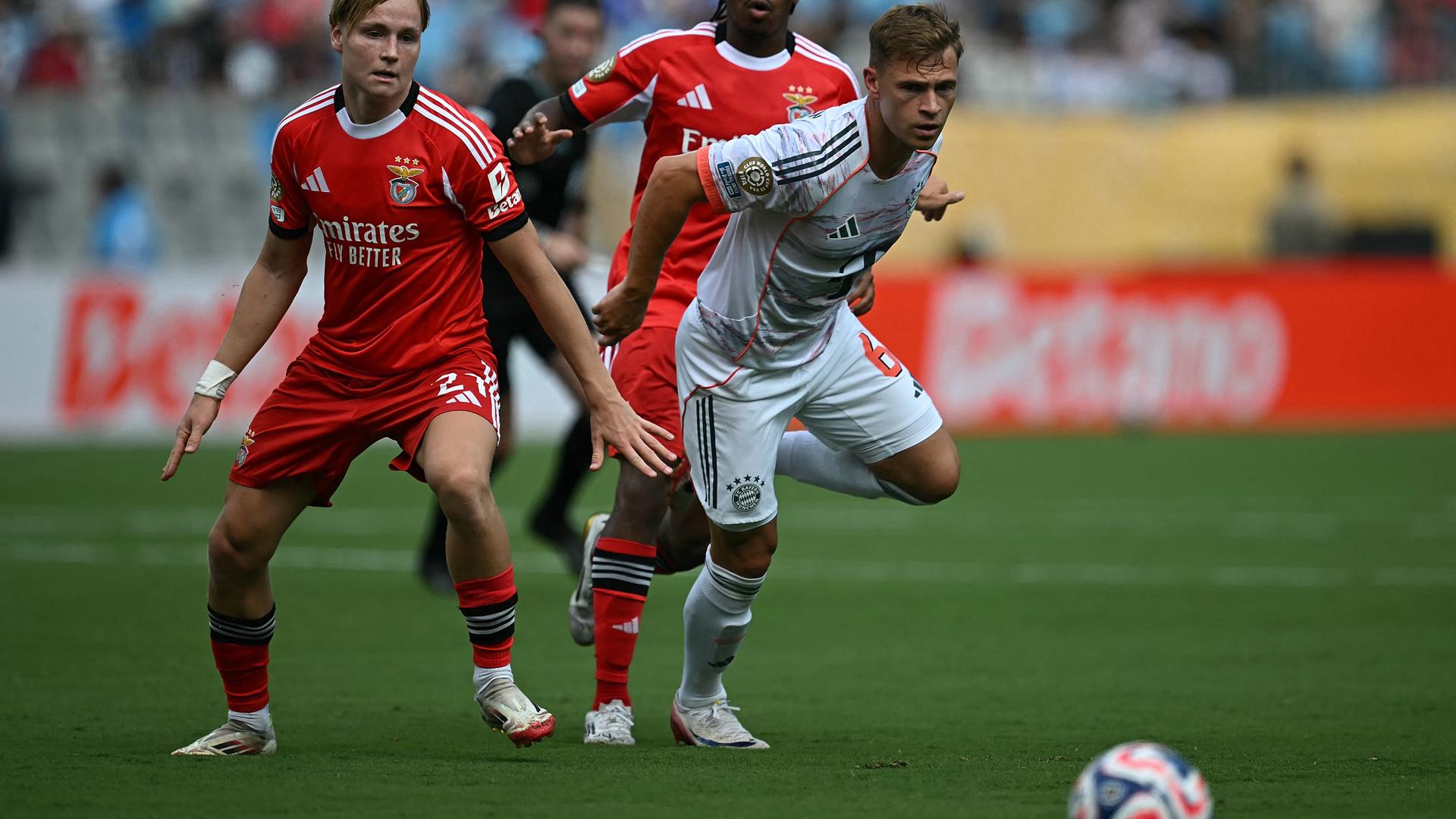 Bayern-Spieler Joshua Kimmich läuft einem Ball hinterher, zwei Benfica-Spieler schauen dabei zu. Bayern-Spieler Joshua Kimmich läuft einem Ball hinterher, zwei Benfica-Spieler schauen dabei zu.