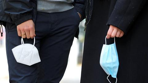 Zwei Personen, die ihre Masken in der Hand baumeln lassen. 