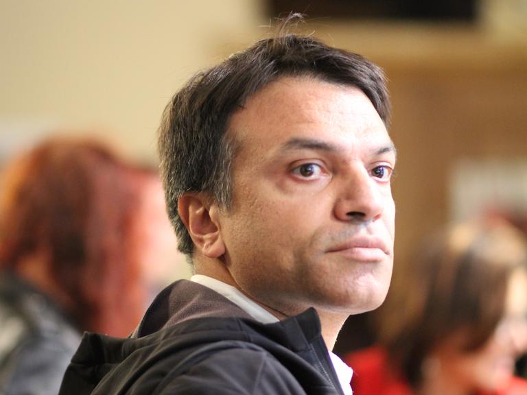 Ein mittelalter Mann im seitlichen Porträt, er hat braune Haare, die an den Schläfen leicht ergrauen, braune Augen und schaut ernst an der Kamera vorbei. Es handelt sich um Hamze Bytyci.