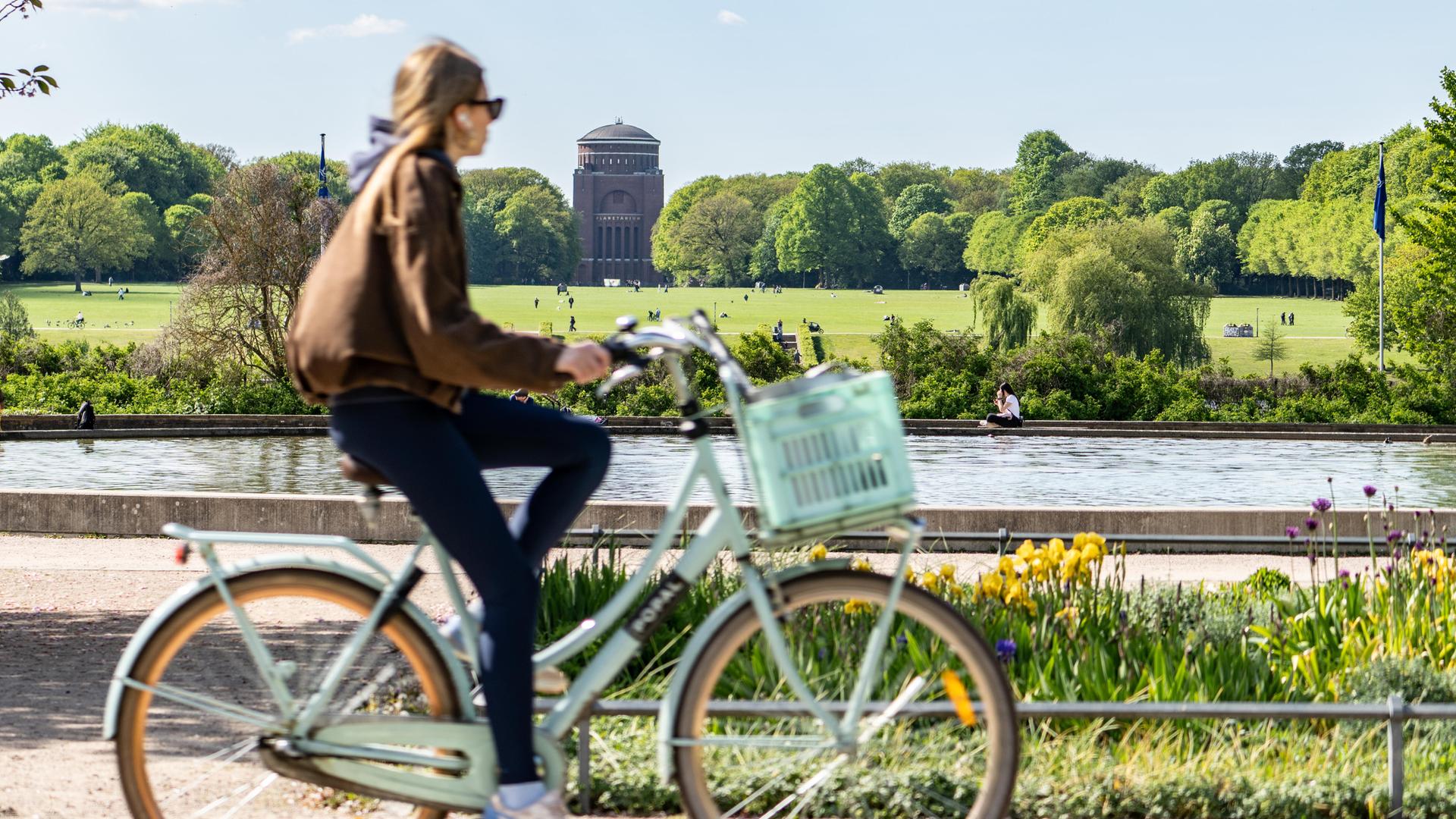 Eine Frau radelt durch den Hamburger Stadtpark. Im Hintergrund eine große Wiese mit Planetarium.