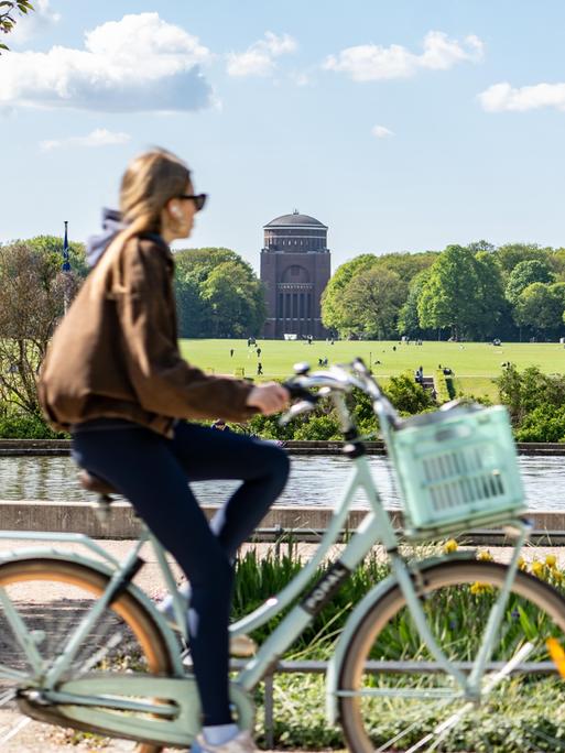 Eine Frau radelt durch den Hamburger Stadtpark. Im Hintergrund eine große Wiese mit Planetarium.