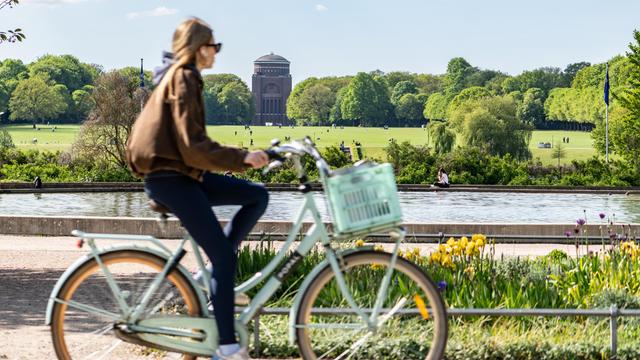 Eine Frau radelt durch den Hamburger Stadtpark. Im Hintergrund eine große Wiese mit Planetarium.