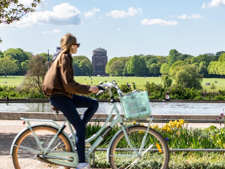 Eine Frau radelt durch den Hamburger Stadtpark. Im Hintergrund eine große Wiese mit Planetarium.