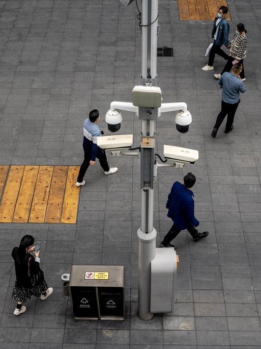 Eine Straßenszene 2023 in Shenzhen, China. Menschen gehen mit ihren Smartphones an zahlreichen Überwachungskameras vorbei.