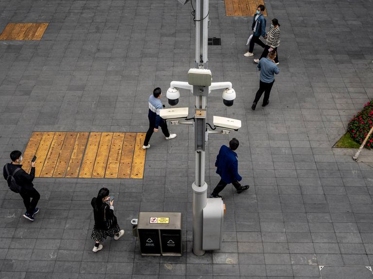 Eine Straßenszene 2023 in Shenzhen, China. Menschen gehen mit ihren Smartphones an zahlreichen Überwachungskameras vorbei.