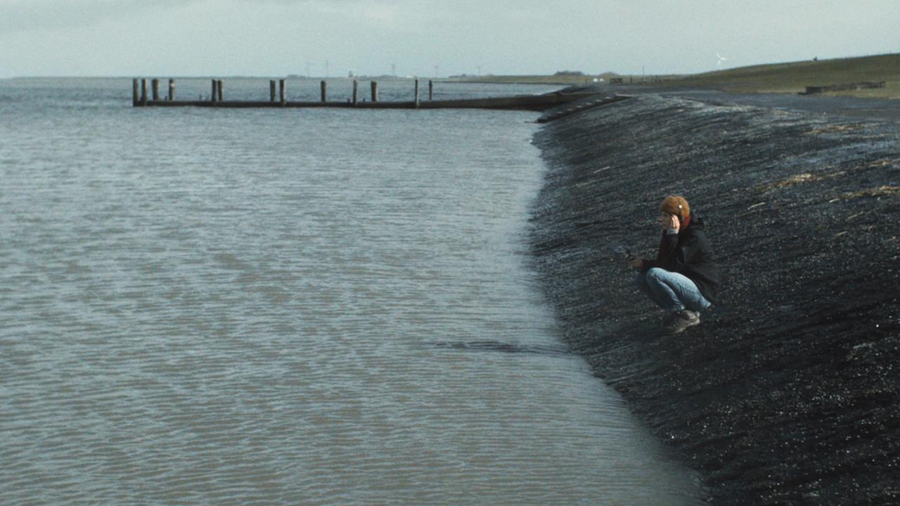 Ein Mädchen sitzt allein am Ufer des Meeres und schaut vor sich hin.
