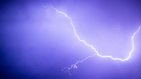 Vor lila-blauem Himmel erstahlt hell ein Blitz. Er erstreckt sich quer über das Bild.