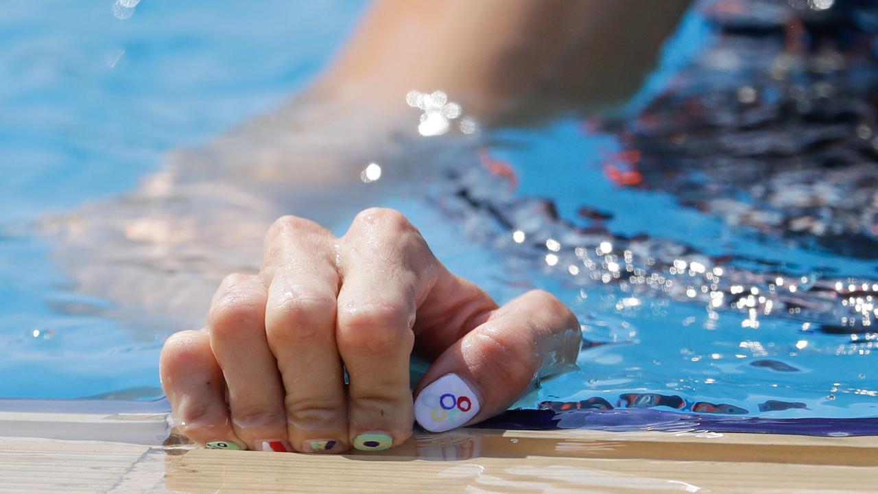 Eine Fünfkampf-Athletin fasst mit ihrer Hand an den Beckenrand. Ihre Nägel sind im Stil der Olympischen Ringe lackiert. 