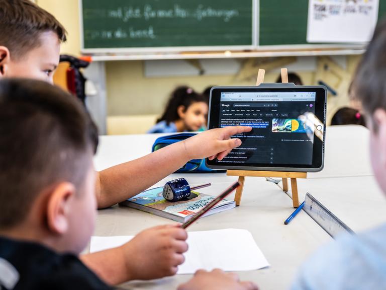 Kinder einer vierten Klasse arbeiten im Unterricht mit einem Tablet