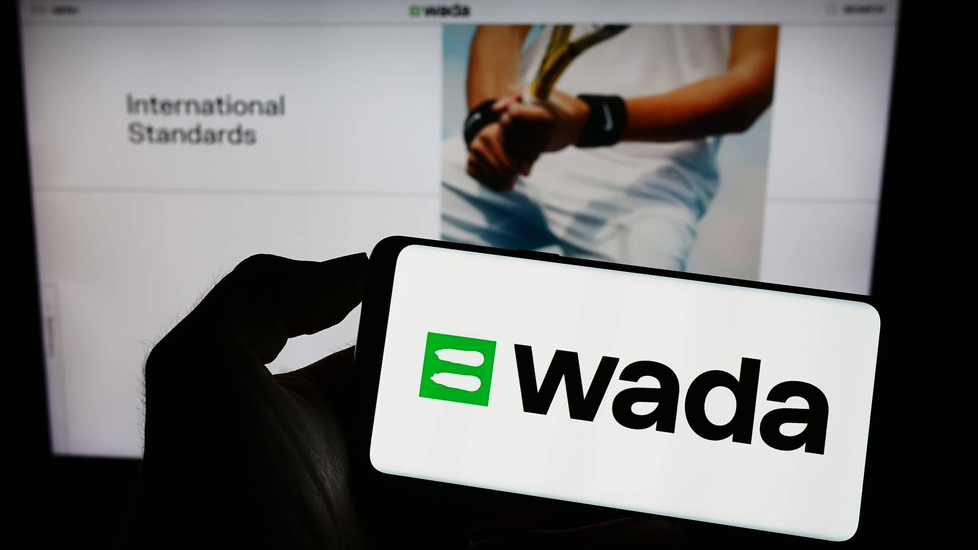 Eine Person hält ein Smartphone mit dem Schriftzug der Welt-Anti-Doping-Agentur (WADA).