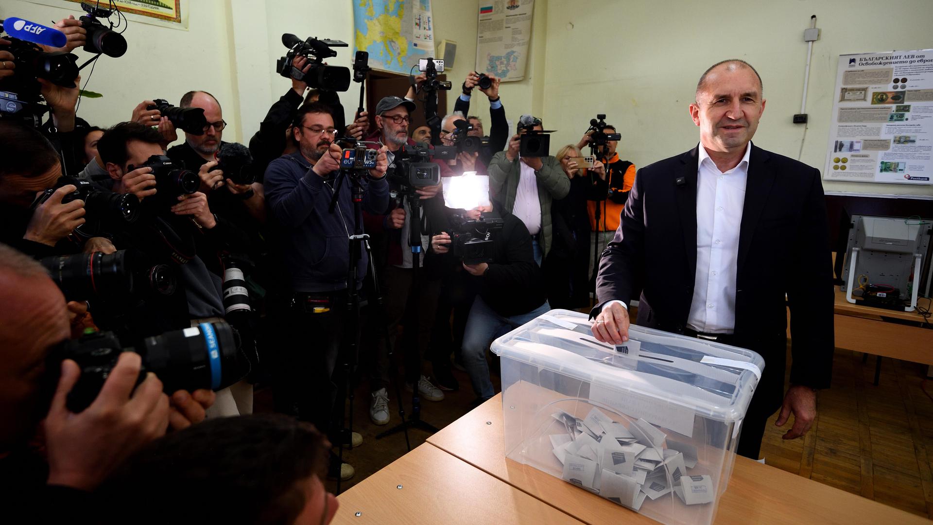 Der frühere bulgarische Präsident Rumen Radew wirft einen Stimmzettel in eine Wahlurne. Neben ihm stehen viele Fotografen.