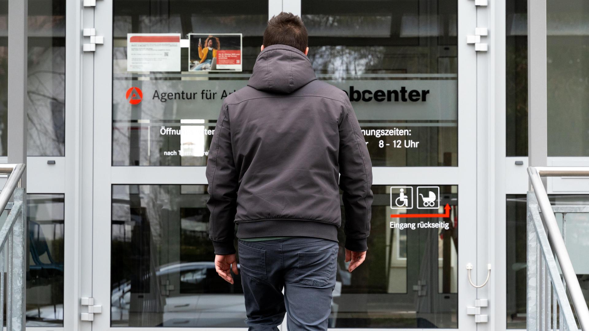 Ein junger Mann steht vor dem Eingang eines Jobcenters.