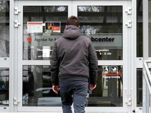 Ein junger Mann steht vor dem Eingang eines Jobcenters.