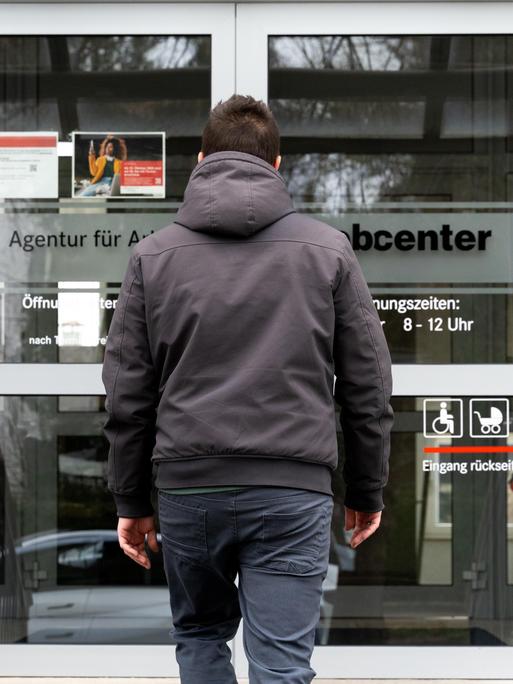 Ein junger Mann steht vor dem Eingang eines Jobcenters.