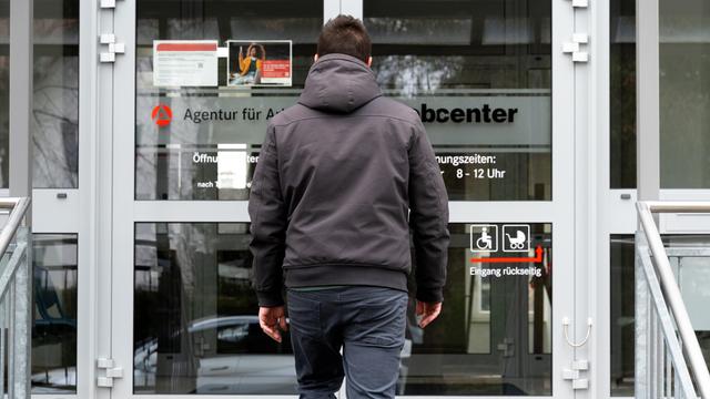 Ein junger Mann steht vor dem Eingang eines Jobcenters.