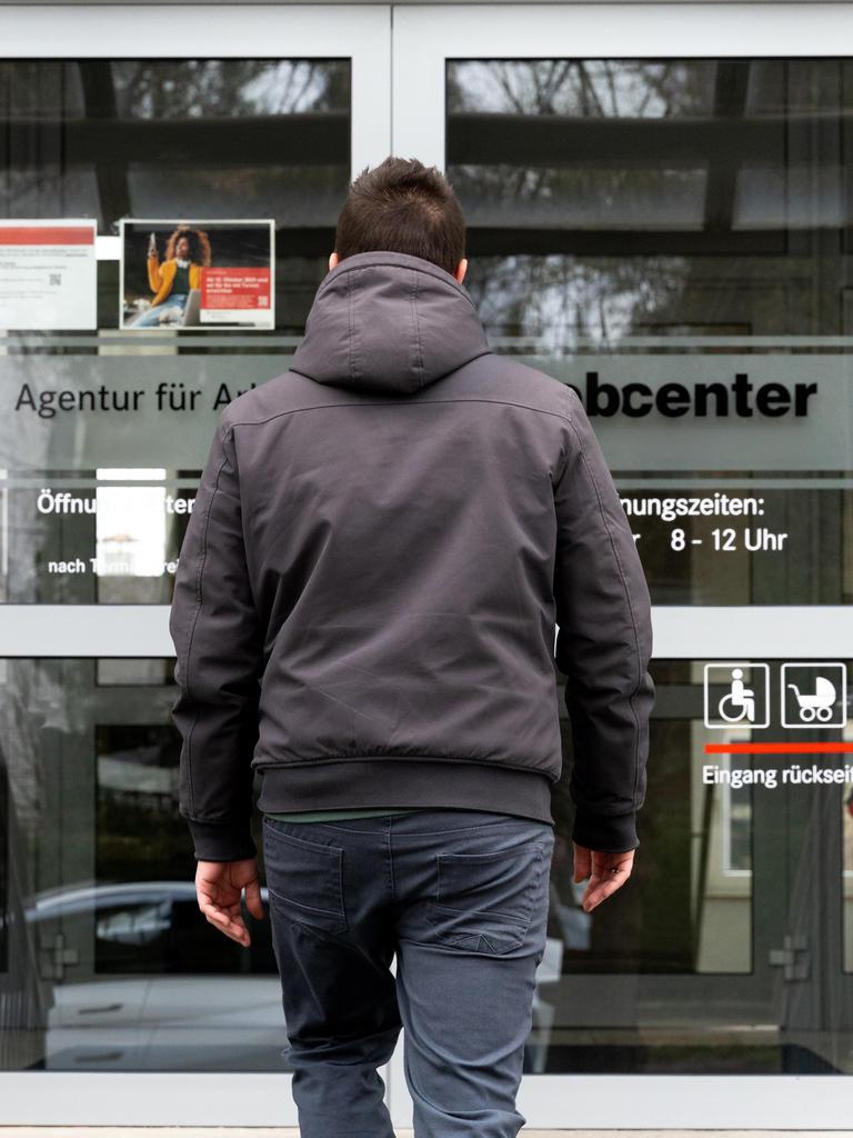 Ein junger Mann steht vor dem Eingang eines Jobcenters.