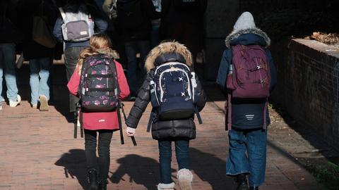 Zu sehen ist eine Gruppe von SchülerInnen mit Schulranzen und Rucksäcken auf dem Rücken beim Laufen durch eine Straße. 