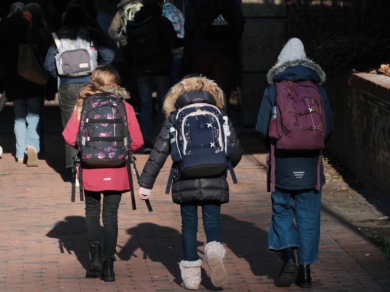 Zu sehen ist eine Gruppe von SchülerInnen mit Schulranzen und Rucksäcken auf dem Rücken beim Laufen durch eine Straße. 