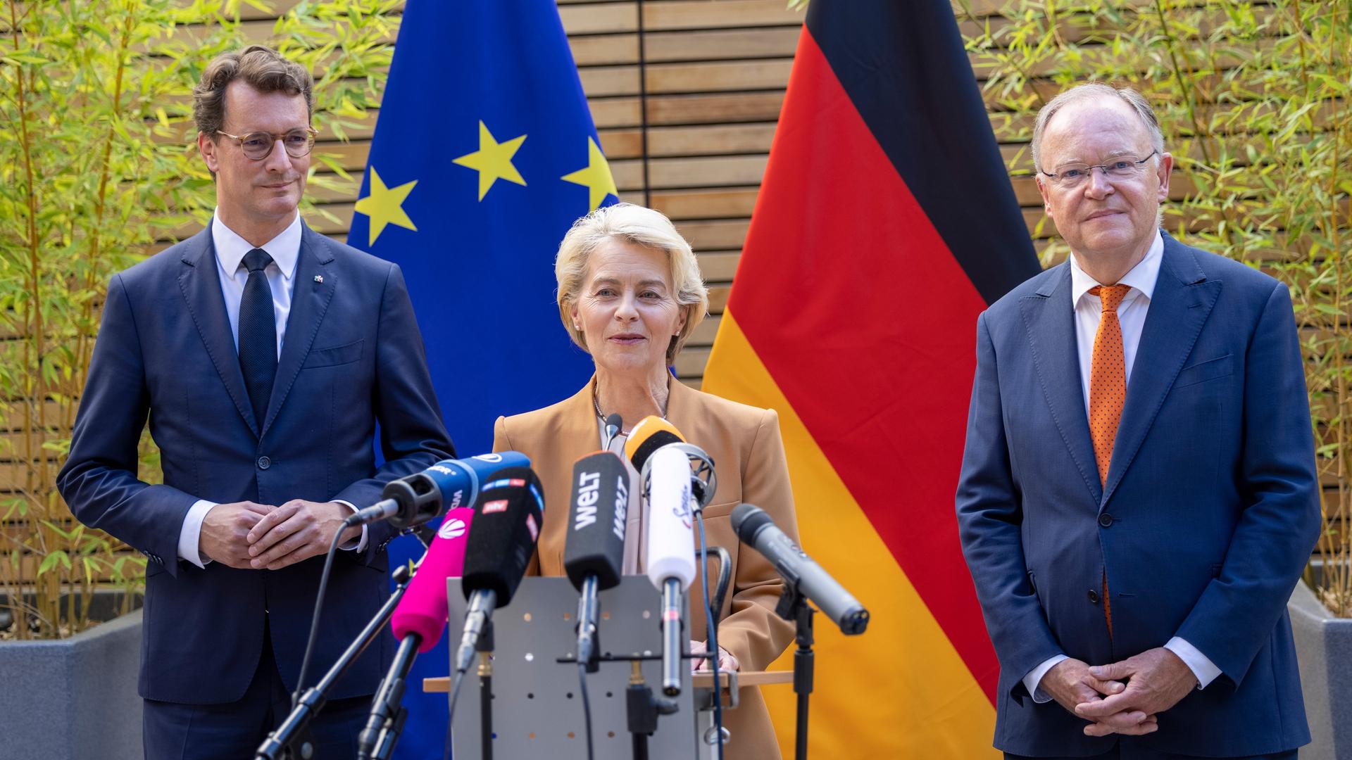 Ursula von der Leyen, Präsidentin der Europäischen Kommission (M), spricht bei einem Statement neben Hendrik Wüst (CDU), Ministerpräsident von Nordrhein-Westfalen, und Stephan Weil (SPD, r), Ministerpräsident von Niedersachsen, in der Vertretung des Landes Niedersachsen bei der Europäischen Union in Brüssel. Im Hintergrund ist eine EU-Fahne und eine Deutschlandfahne zu sehen. Ursula von der Leyen, Präsidentin der Europäischen Kommission (M), spricht bei einem Statement neben Hendrik Wüst (CDU), Ministerpräsident von Nordrhein-Westfalen, und Stephan Weil (SPD, r), Ministerpräsident von Niedersachsen, in der Vertretung des Landes Niedersachsen bei der Europäischen Union in Brüssel. Im Hintergrund ist eine EU-Fahne und eine Deutschlandfahne zu sehen.