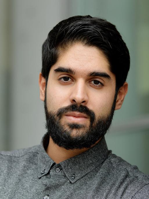 Emran Feroz schaut in die Kamera. Er trägt dunkles Haar mit einem gestutzten Vollbart und ein graues Kragenhemd.