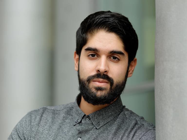 Emran Feroz schaut in die Kamera. Er trägt dunkles Haar mit einem gestutzten Vollbart und ein graues Kragenhemd.