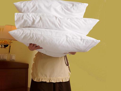 Eine Person mit Schürze hält drei Kopfkissen vor ihren Körper.
