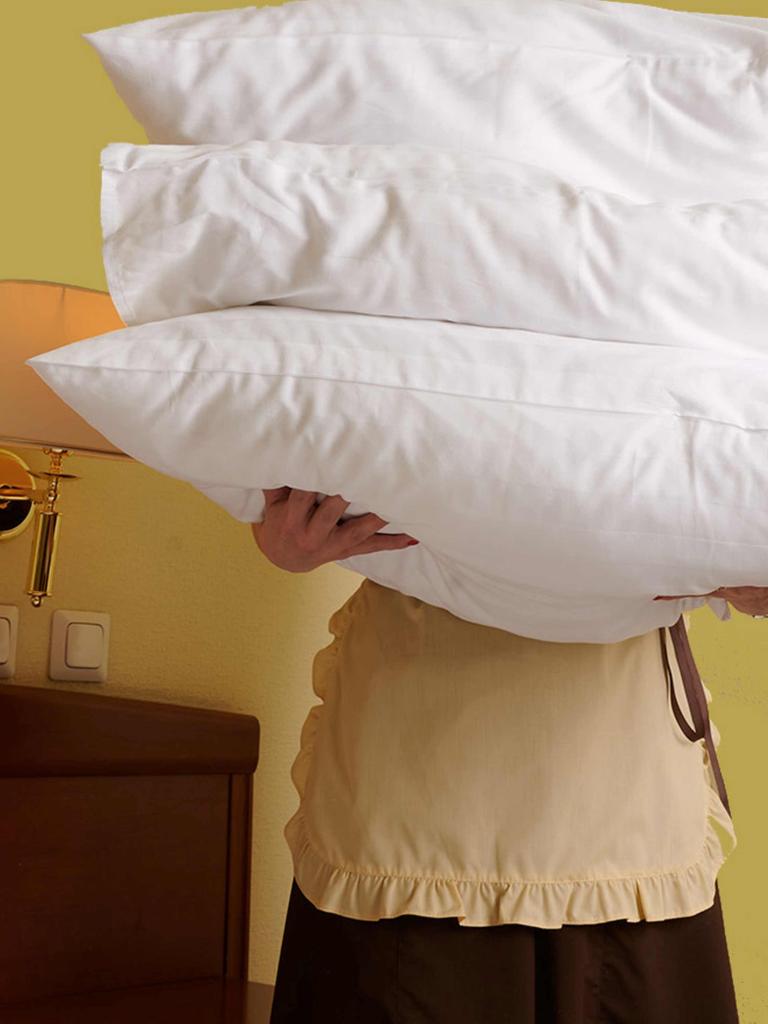 Eine Person mit Schürze hält drei Kopfkissen vor ihren Körper.