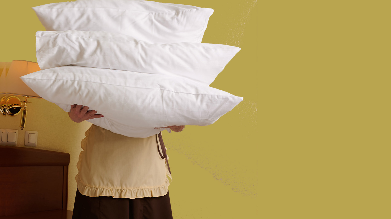 Eine Person mit Schürze hält drei Kopfkissen vor ihren Körper.