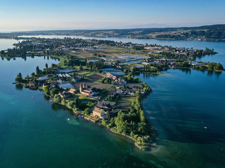 Die aufgehende Sonne strahlt die romanische Säulenbasilika, St. Peter und Paul, auf der Insel Reichenau an. Aufnahme mit Drohne.