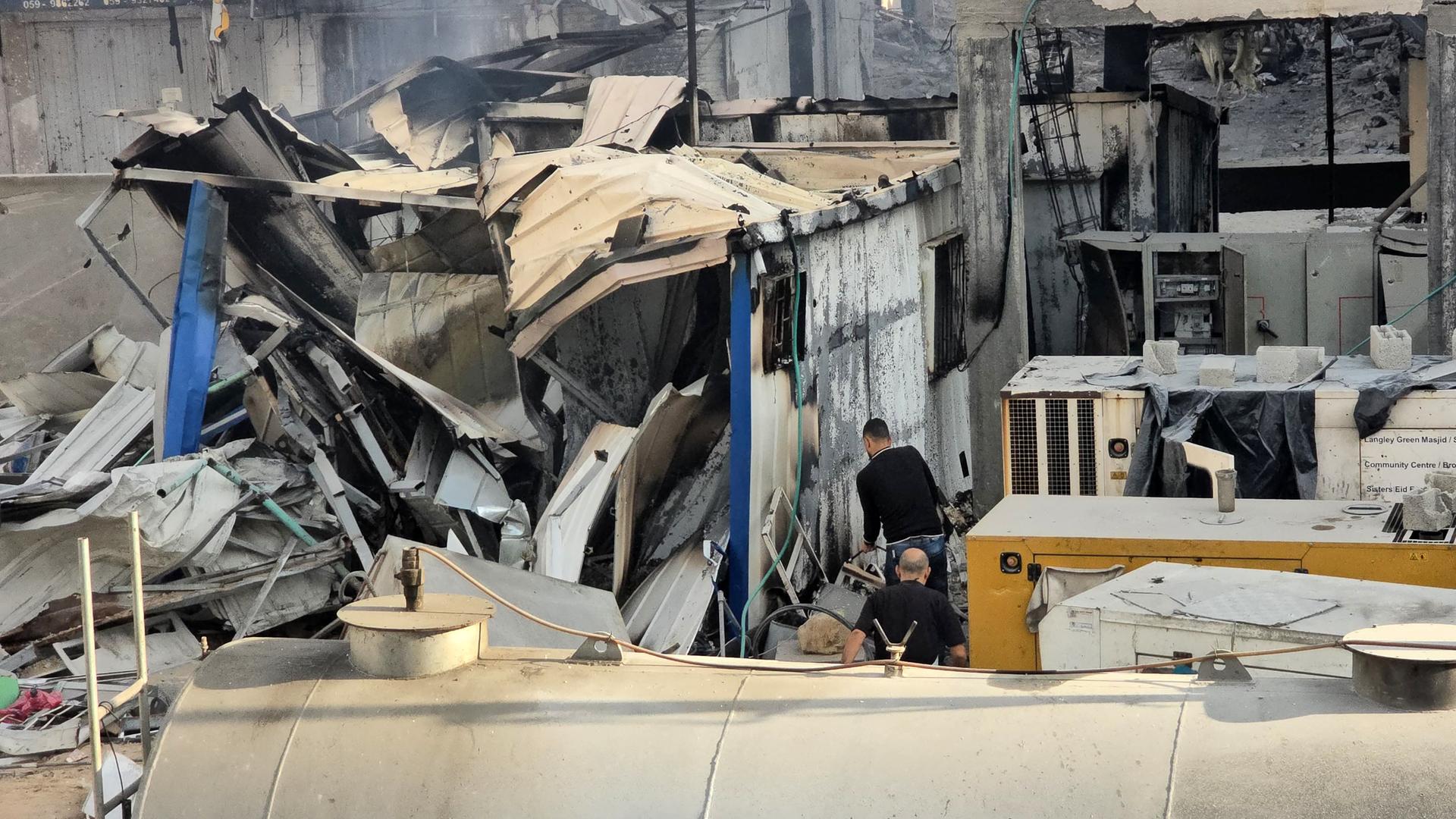 Mehrere zerstörte Container in einem Hof des Krankenhauses, mittendrin zwei Männer. 