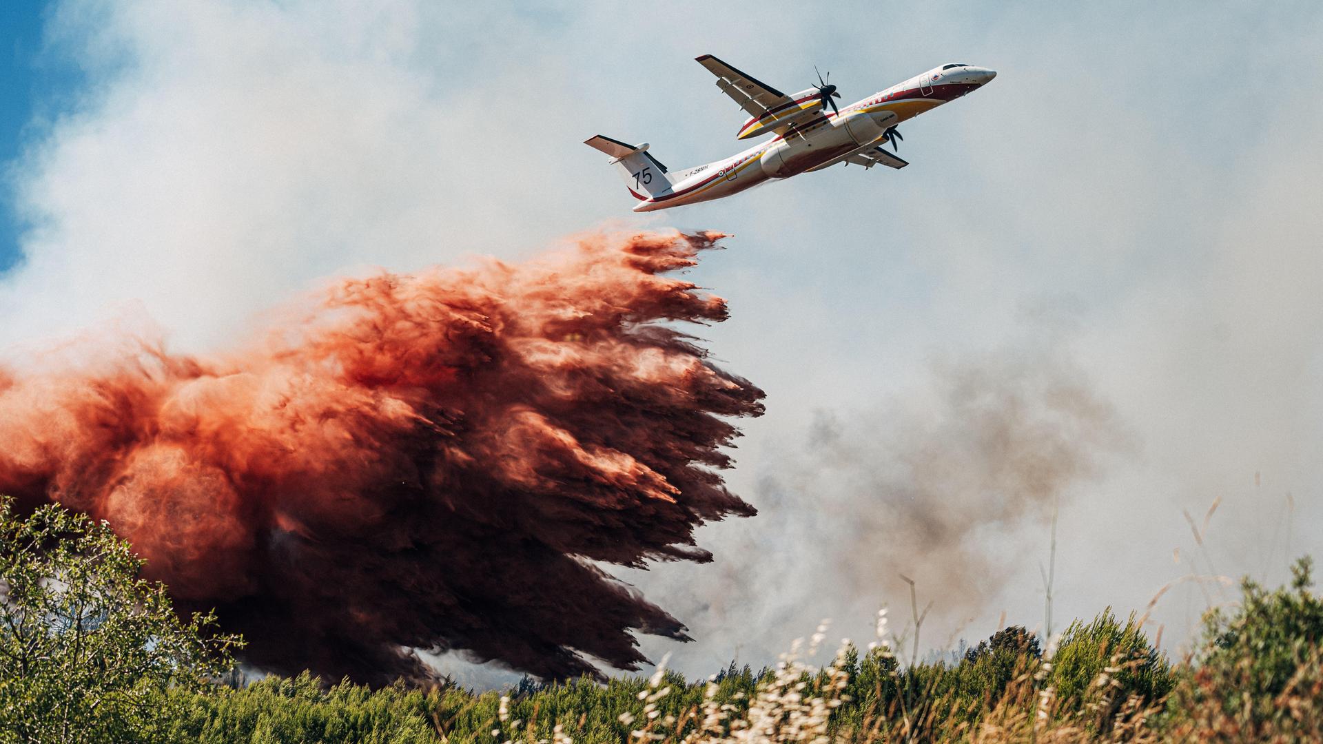 Ein Löschflugzeug überfliegt eine brennende Fläche und wirft Löschmaterial ab. 
