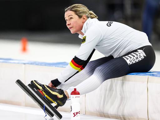 Claudia Pechstein bindet sitzend ihre Schlittschuhe bei der Eisschnelllauf-WM in Herenveen 2023.