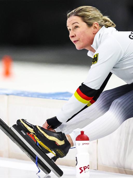 Claudia Pechstein bindet sitzend ihre Schlittschuhe bei der Eisschnelllauf-WM in Herenveen 2023.