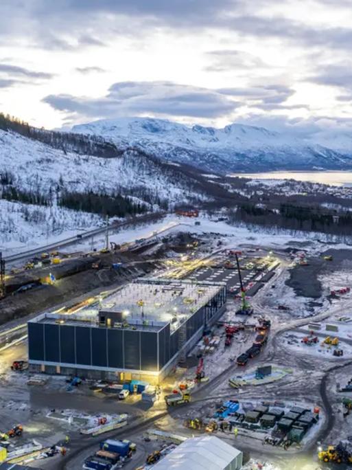 Eine Drohnenaufnahme des neu gebauten KI-Rechenzentrums in Narvik, Norwegen bei Dämmerung. Im Hintergrund schneebedeckte Berge und ein Fjord